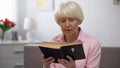 Religious senior woman reading holy bible at home, faith and belief concept