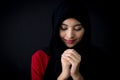 Religious young Muslim woman praying over black background.