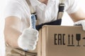 Relocation services concept. Loader in uniform shows thumb up closeup. Mover with cardboard box. Delivery man carrying moving box
