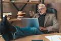 Reluctance to work. Senior man sits with laptop, legs propped up on desk in office. Procrastination Royalty Free Stock Photo