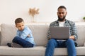 Reluctant Black Dad Ignoring Offended Son Using Laptop Indoors