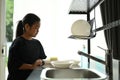 A reluctant little girl is looking at dirty dishes in kitchen.