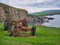 The remains of an abandoned, rusted tractor in a grassy field on the coast near Bigton, Shetland, UK