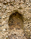 Remains of arched recess in a medieval wall made with weathered flint stone,