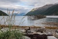 Remains of a pier at the beach with grass and seaweed surrounded by mountains Royalty Free Stock Photo