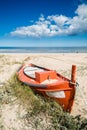 Remains of a small orange boat covered with plants and sand on the beach. Partly cloudy sky. Portrait orientation