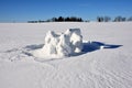 The remains of a snow fort created by kids under the bright sun on the background of snowy field, forest and blue sky in winter in