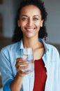 Remember to drink your eight glasses daily. Portrait of a woman drinking a glass of water at home.