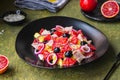 Remojon salad of blood oranges, potatoes, boiled salted fish and red onions on a black plate on a green concrete background.