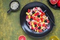 Remojon salad of blood oranges, potatoes, boiled salted fish and red onions on a black plate on a green concrete background.