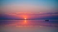 A remote boat in the quiet sea on picturesque sunset background.