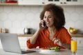 Remote Business. Black Woman Using Cellphone And Working On Laptop In Kitchen Royalty Free Stock Photo
