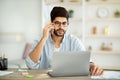 Remote business. Concentrated arab male freelancer talking on cellphone and working on laptop at home office Royalty Free Stock Photo