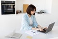 Remote business. Young freelancer lady working on laptop in kitchen, sitting at table and typing on pc keyboard Royalty Free Stock Photo