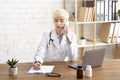 Remote consultation and call to family doctor. Busy adult lady therapist talking on phone and taking notes in tablet Royalty Free Stock Photo