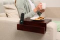 Remote control and cookies on sofa armrest wooden table. Woman holding cup of drink at home, closeup Royalty Free Stock Photo