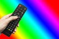 Remote control in hand against a bright rainbow background