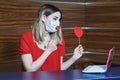 Remote dating during quarantine. Virtual love on Valentine's Day. Girl in medical mask with a paper heart during