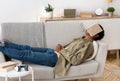 Remote education concept. Bored black teen student with book on his face sleeping on couch at home