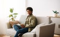 Remote education concept. Joyful African American student reading book on comfy couch at home Royalty Free Stock Photo