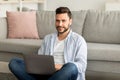 Remote job concept. Successful young freelancer man working on laptop, sitting on floor, working remotely from home Royalty Free Stock Photo