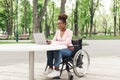 Remote job for people with disability. Young black woman in wheelchair working online, using laptop at outdoor cafe Royalty Free Stock Photo