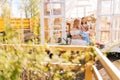 Remote view of cheerful blonde young mother in dress sitting on doorstep of summer gazebo house with two little adorable Royalty Free Stock Photo