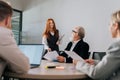 Remote view of cheerful female colleague come in for business briefing and take seat at table with mature adult business Royalty Free Stock Photo