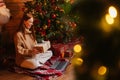 Cheerful young woman holding gift box while having video call on laptop near Christmas tree. Royalty Free Stock Photo