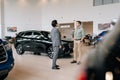 Remote view of doubtful male customer buying car in showroom talking to sales agent in business suit looking at auto Royalty Free Stock Photo