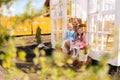 Remote view of elegance blonde young mother in dress sitting on doorstep of summer gazebo house with two little adorable Royalty Free Stock Photo