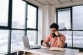 Remote view of handsome Indian businessman in glasses using smartphone sitting at office desk with laptop and paper Royalty Free Stock Photo