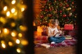 Remote view of smiling charming little blonde curly child girl writing letter to Santa Claus sitting on floor sitting by Royalty Free Stock Photo