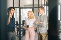 Remote view of three young business people having fun conversation during coffee break in modern office. Happy coworkers Royalty Free Stock Photo