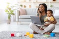 Remote Work With Baby. Black Mom Using Laptop And Talking On Cellphone Royalty Free Stock Photo