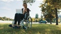 Remote work concept. Young disabled woman in the wheelchair using smartphone and laptop Royalty Free Stock Photo