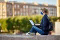 Young woman uses laptop to work remotely outdoors during coronavirus lockdown.