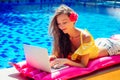 Remote work dream job.young woman sitting on inflatable pink mattress in the swimming pool having sunbath and working on