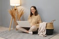 Remote work on laptop. Internet-based freelancing. Satisfied Caucasian woman freelancer wearing beige jumper working on computer