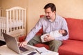 Working from home with kids: father in grey shirt sitting on sofa, holding in one hand infant baby and typing on laptop keyboard Royalty Free Stock Photo