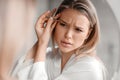 Removal of excess hair from face. Young woman in sleepwear plucking eyebrows in bathroom interior, closeup