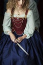 A Renaissance woman wearing a red brocade corset and blue silk skirt and holding a dagger Royalty Free Stock Photo