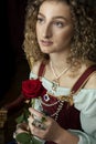 A Renaissance woman wearing a red brocade corset and blue silk skirt and holding a red rose Royalty Free Stock Photo