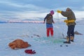 A mongolian couple is fishing through a hole in a frozen lake