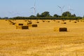 Renewable energy wind turbines behind a freshly harvested agricultural field with square hay bales Royalty Free Stock Photo