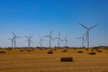 Renewable energy wind turbines behind a freshly harvested agricultural field with square hay bales Royalty Free Stock Photo