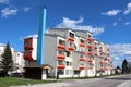 Renovated and completely restored small apartment building with new facade and tall blue chimney surrounded with grass and paved