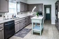 A renovated kitchen in an older home with painted gray cabinets, marble countertops, a small portable island and a tiled