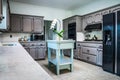 A renovated kitchen in an older home with painted gray cabinets, marble countertops, a small portable island and a tiled