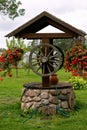 Renovated old classic water well. The well, which is decorated with flower pots with red begonia